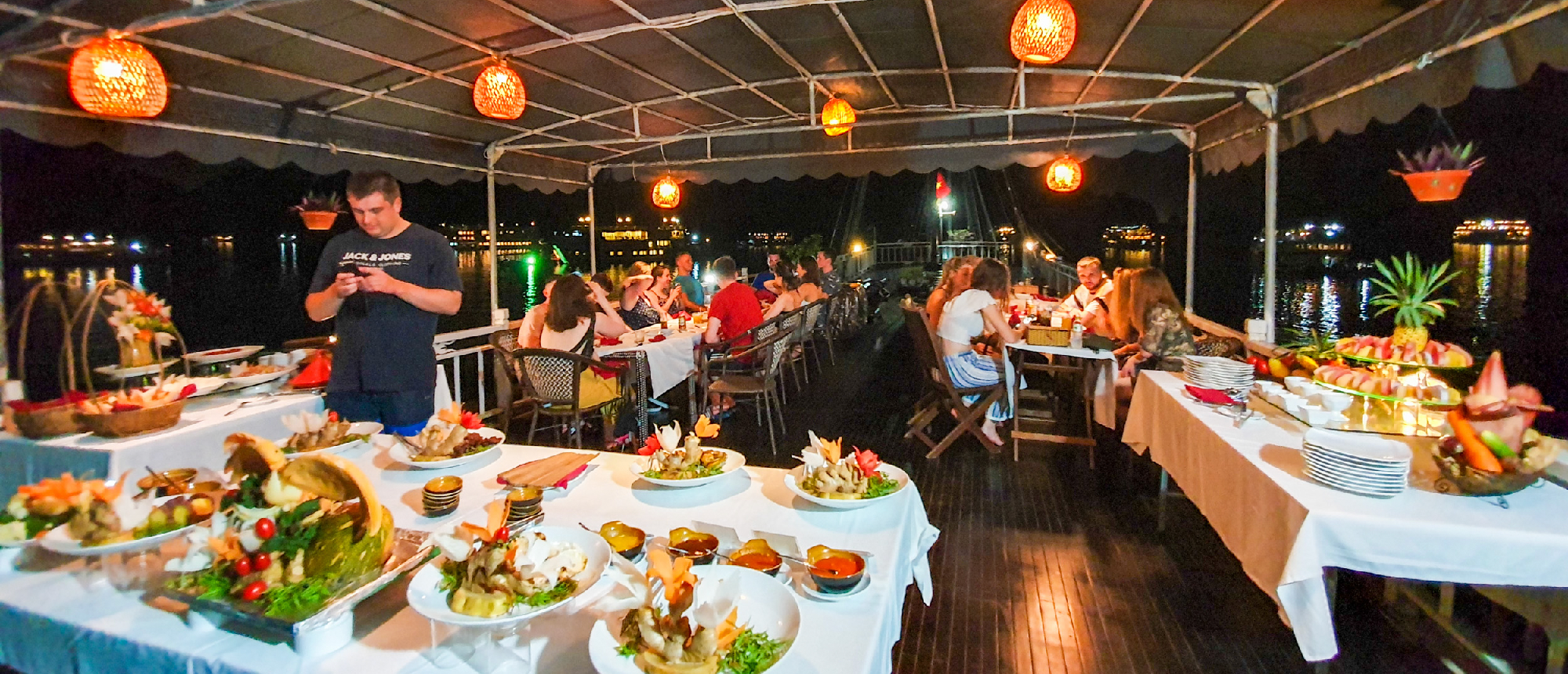 Tourists enjoy a lavish buffet dinner on a boat cruise in Halong Bay at night.