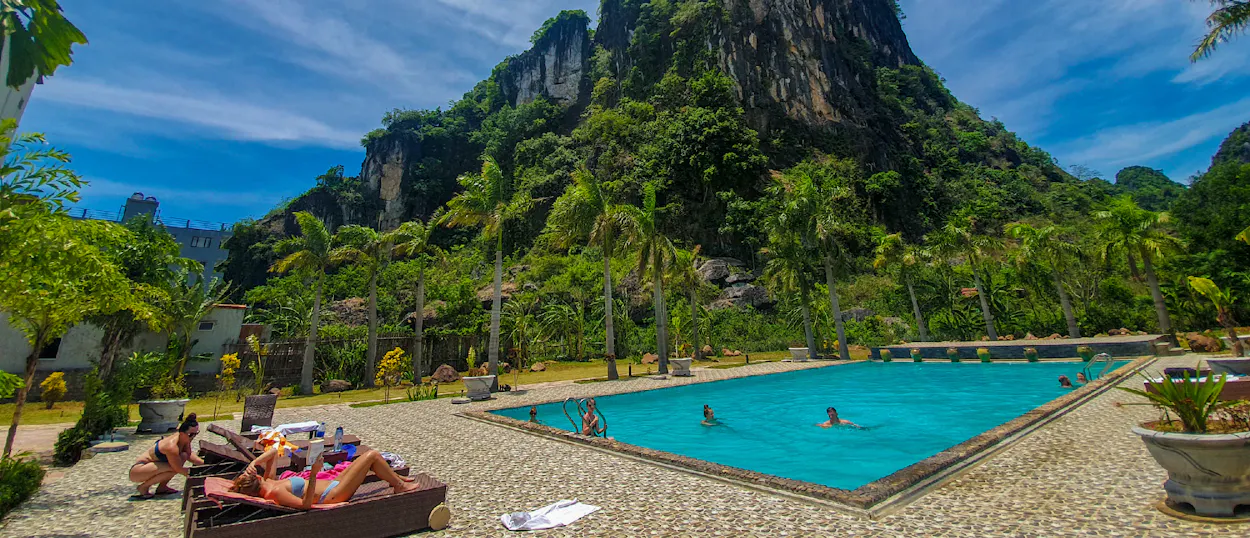 People swim and sunbathe in a pool surrounded by dramatic karst mountains in Phong Nha, Vietnam.