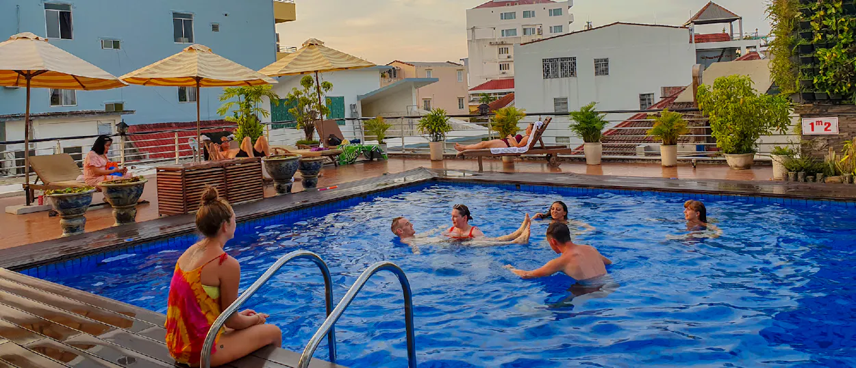 Travelers relax and swim in a rooftop pool at sunset, surrounded by urban buildings in Hue.