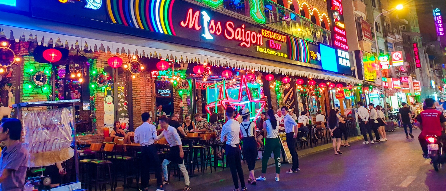 A vibrant Ho Chi Minh City street at night, bustling with people, neon signs, and red lanterns.