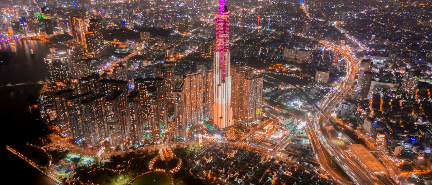 Aerial view of Ho Chi Minh City at night, with the Landmark 81 skyscraper glowing pink and orange.