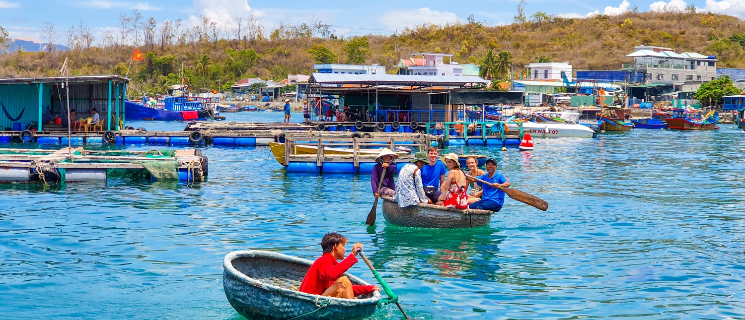 People paddle traditional Vietnamese basket boats on blue water near floating structures in Nha Trang.