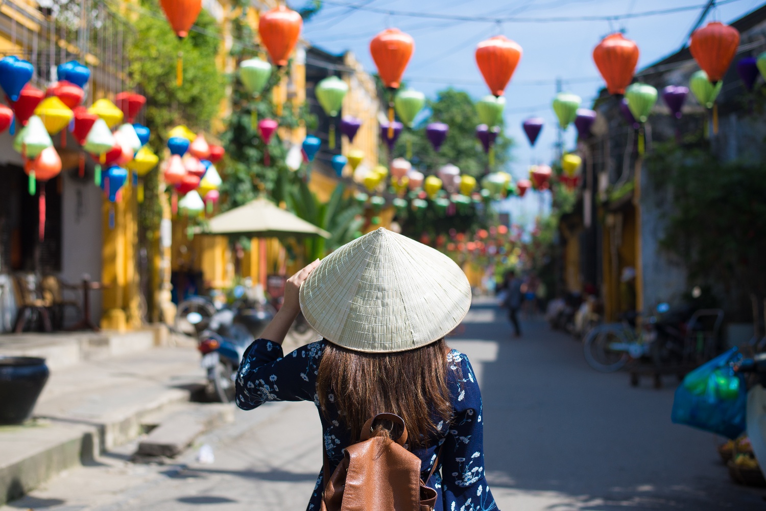 Woman in a conical hat exploring a vibrant Vietnamese street adorned with colorful lanterns.