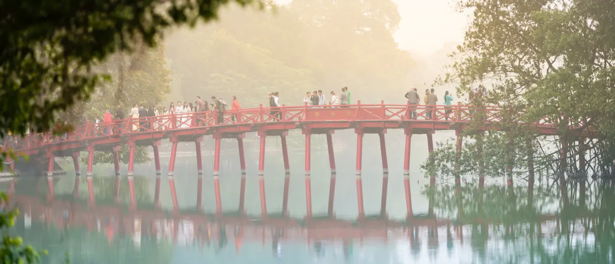 People stroll across the iconic red Huc Bridge over Hoan Kiem Lake in Hanoi, Vietnam, on a misty morning.