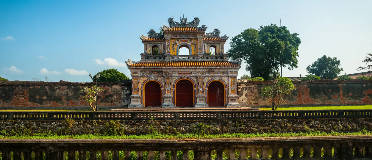 Ornate imperial gate with three red doors and yellow roofs, surrounded by ancient walls in Hue.
