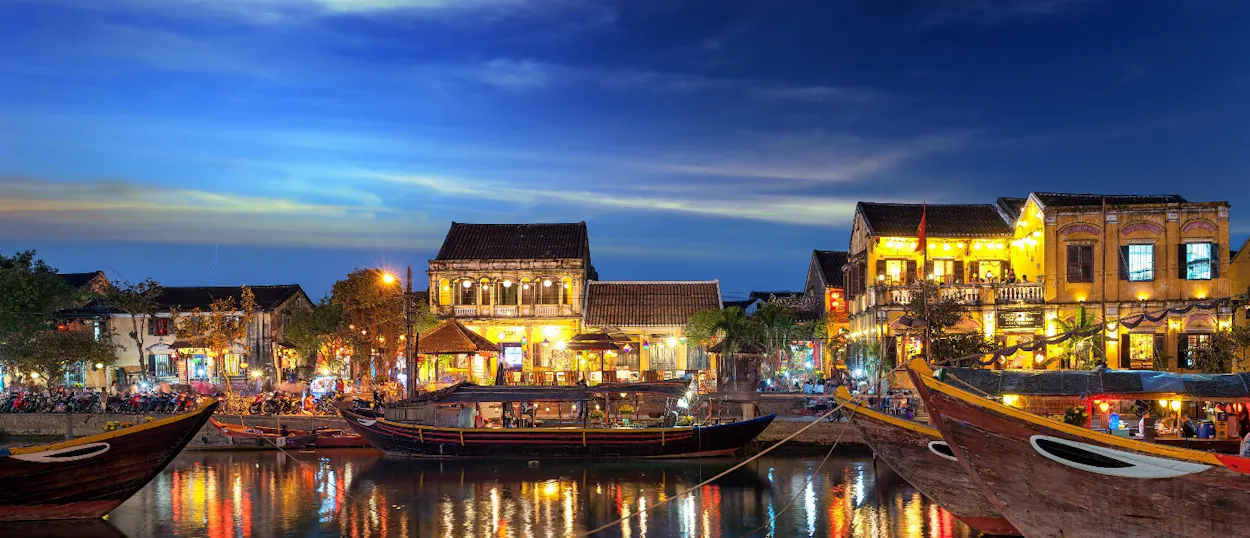 Vibrant Hoi An at night, with glowing lanterns, historic buildings, and boats on the tranquil river.