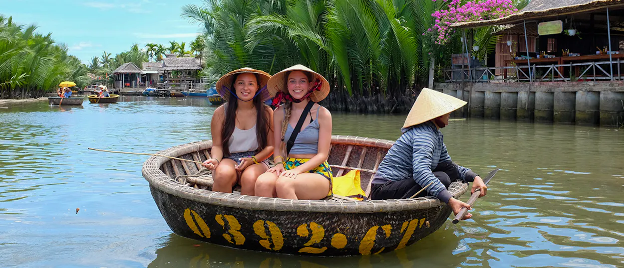 Two women in conical hats enjoy a basket boat ride with a local guide through coconut groves in Hoi An.