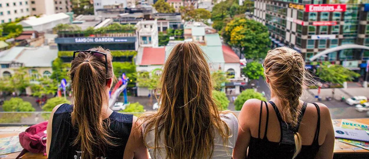 Three friends look out over a vibrant city skyline from a high vantage point.