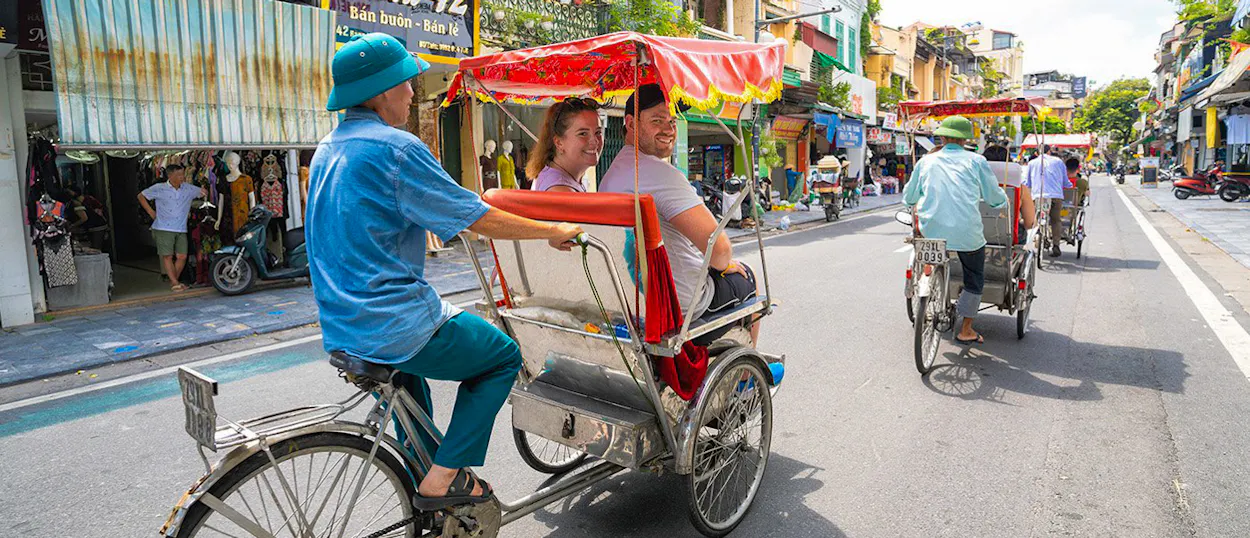 Tourists ride a traditional rickshaw through a bustling street in Hanoi, enjoying the vibrant city life.