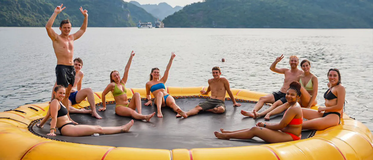 Joyful travelers wave from a floating trampoline in the beautiful emerald waters of Ha Long Bay.