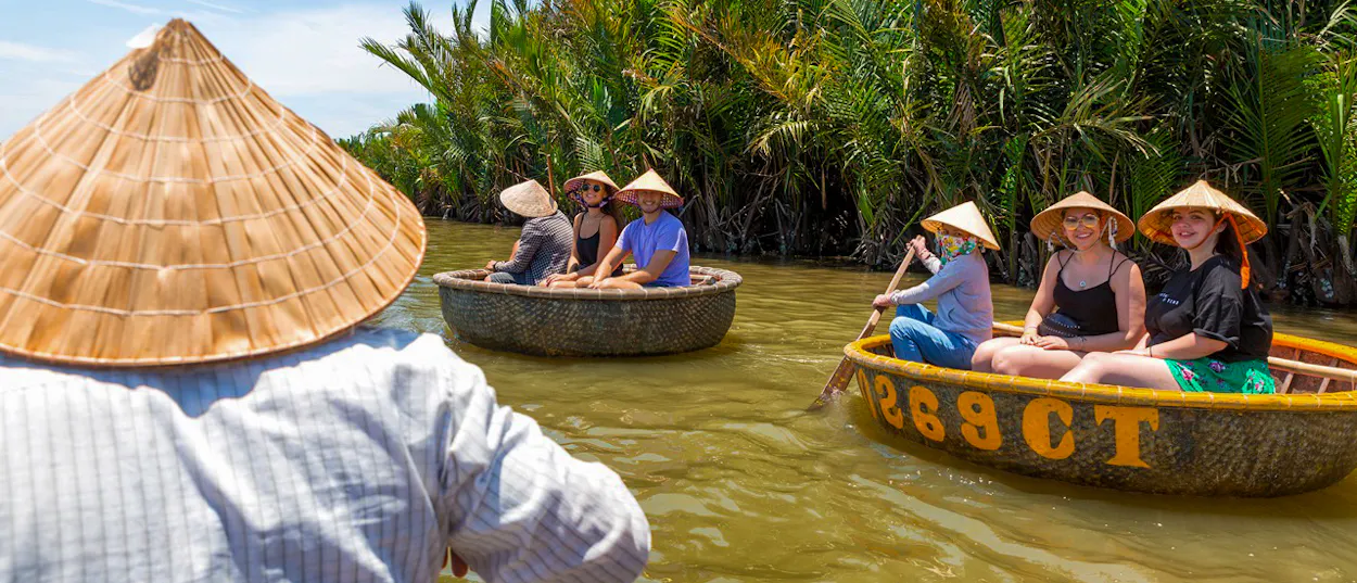 Travelers in conical hats enjoy a traditional basket boat ride through lush coconut groves in Hoi An.