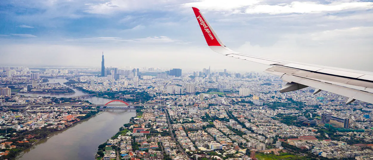 Bustling Ho Chi Minh City from an airplane, with a river, red bridge, and towering skyscrapers.