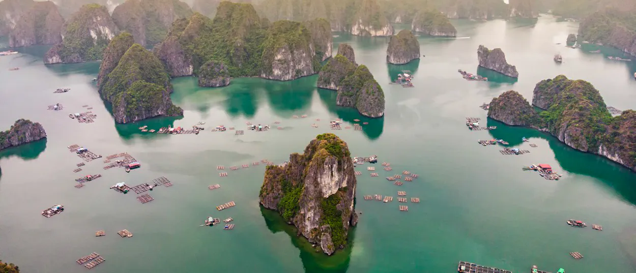 Towering limestone karsts rise from emerald waters, surrounded by floating villages in Ha Long Bay.