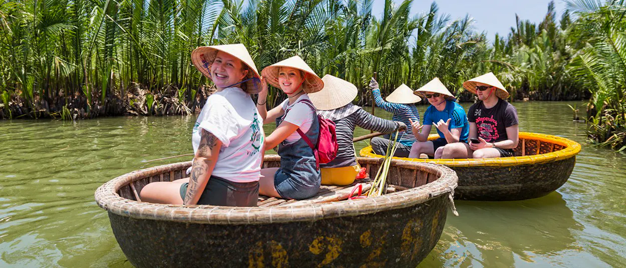 Happy tourists in conical hats navigate traditional basket boats through Hoi An's lush coconut groves.