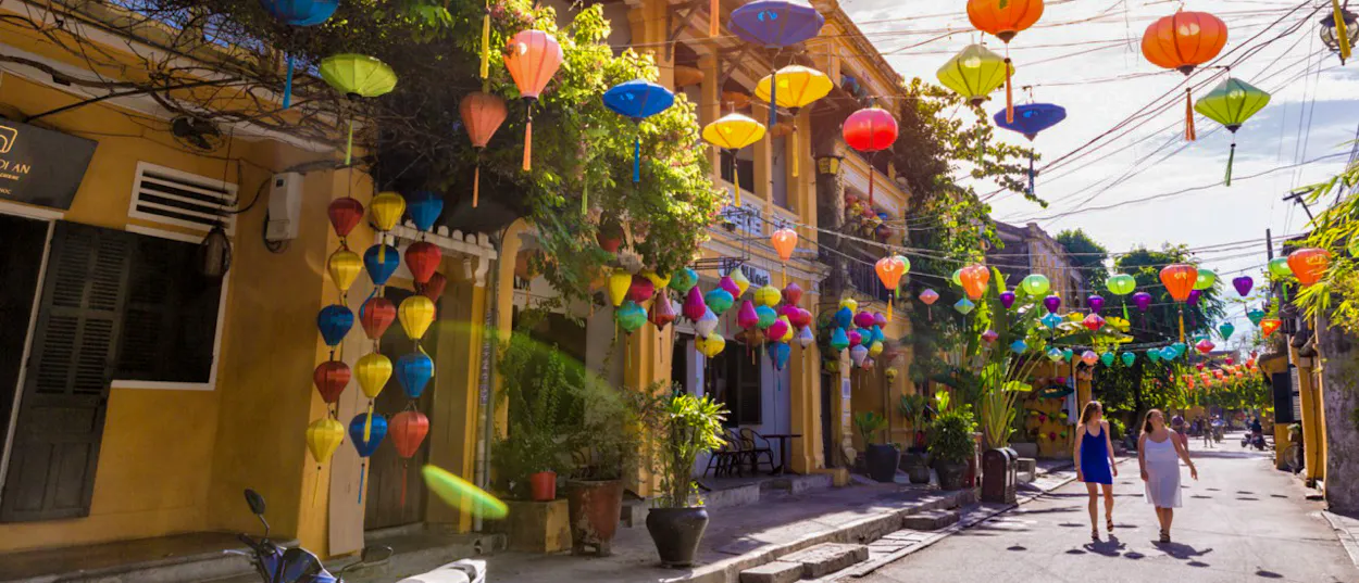 Two women walk along a charming Hoi An street decorated with many colorful lanterns and umbrellas.