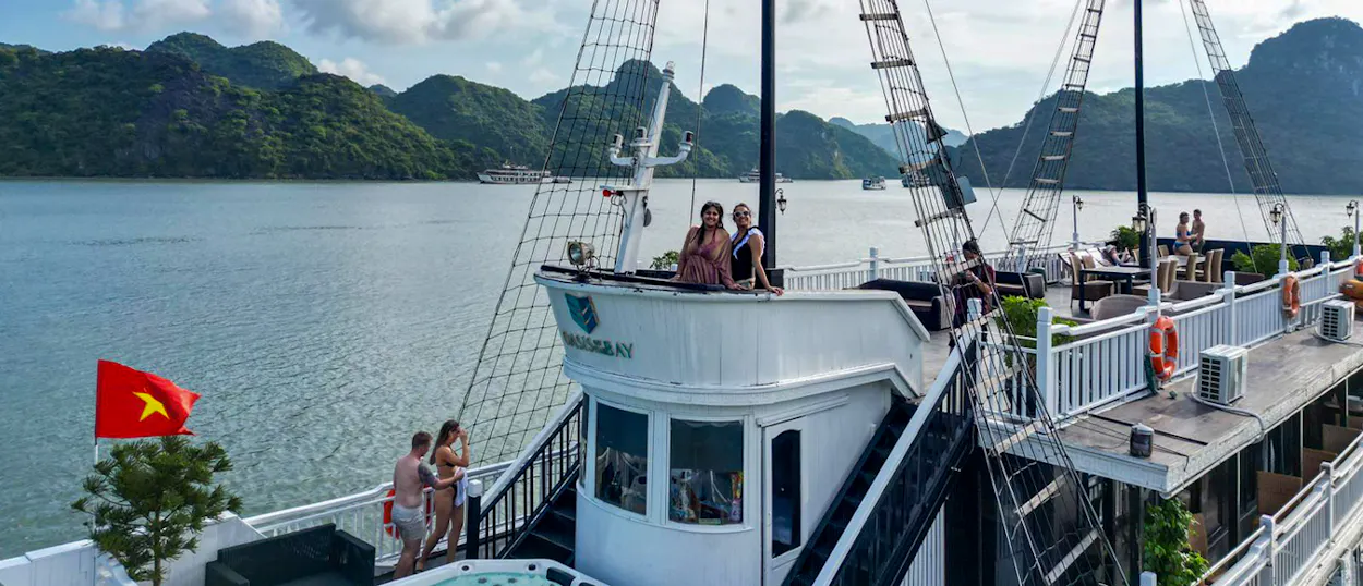 Travelers relax on a cruise boat with a hot tub, surrounded by majestic limestone karsts in Ha Long Bay.