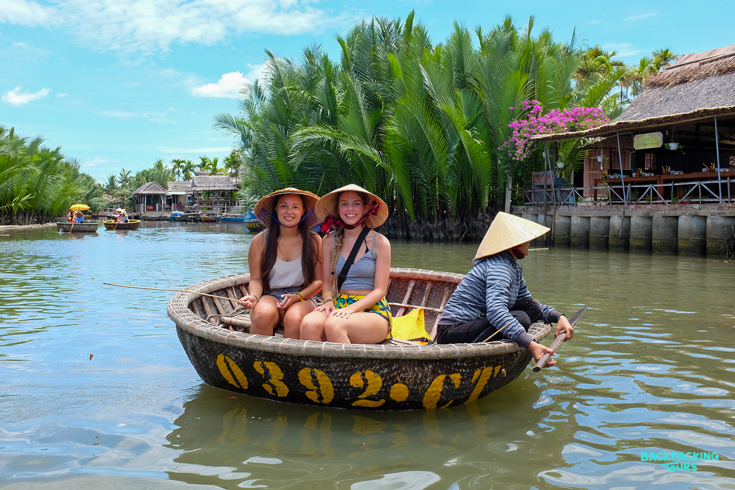 Two smiling women in conical hats on a traditional basket boat ride through Hoi An's coconut groves.