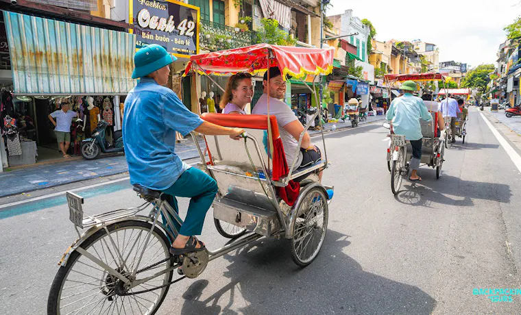 Two tourists enjoy a traditional rickshaw ride through the bustling streets of Hanoi.