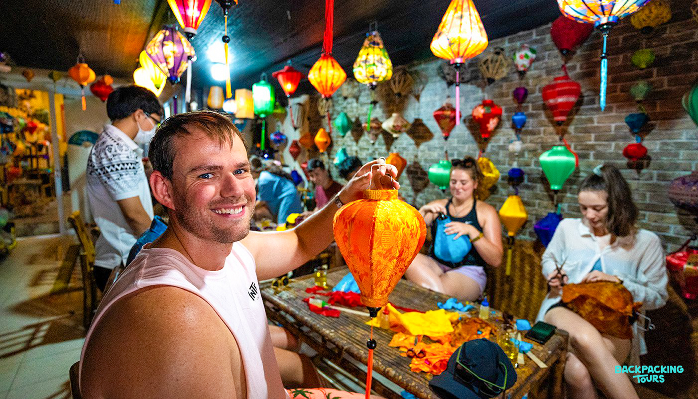 Tourists happily making colorful handmade lanterns in a vibrant workshop in Hoi An, Vietnam.