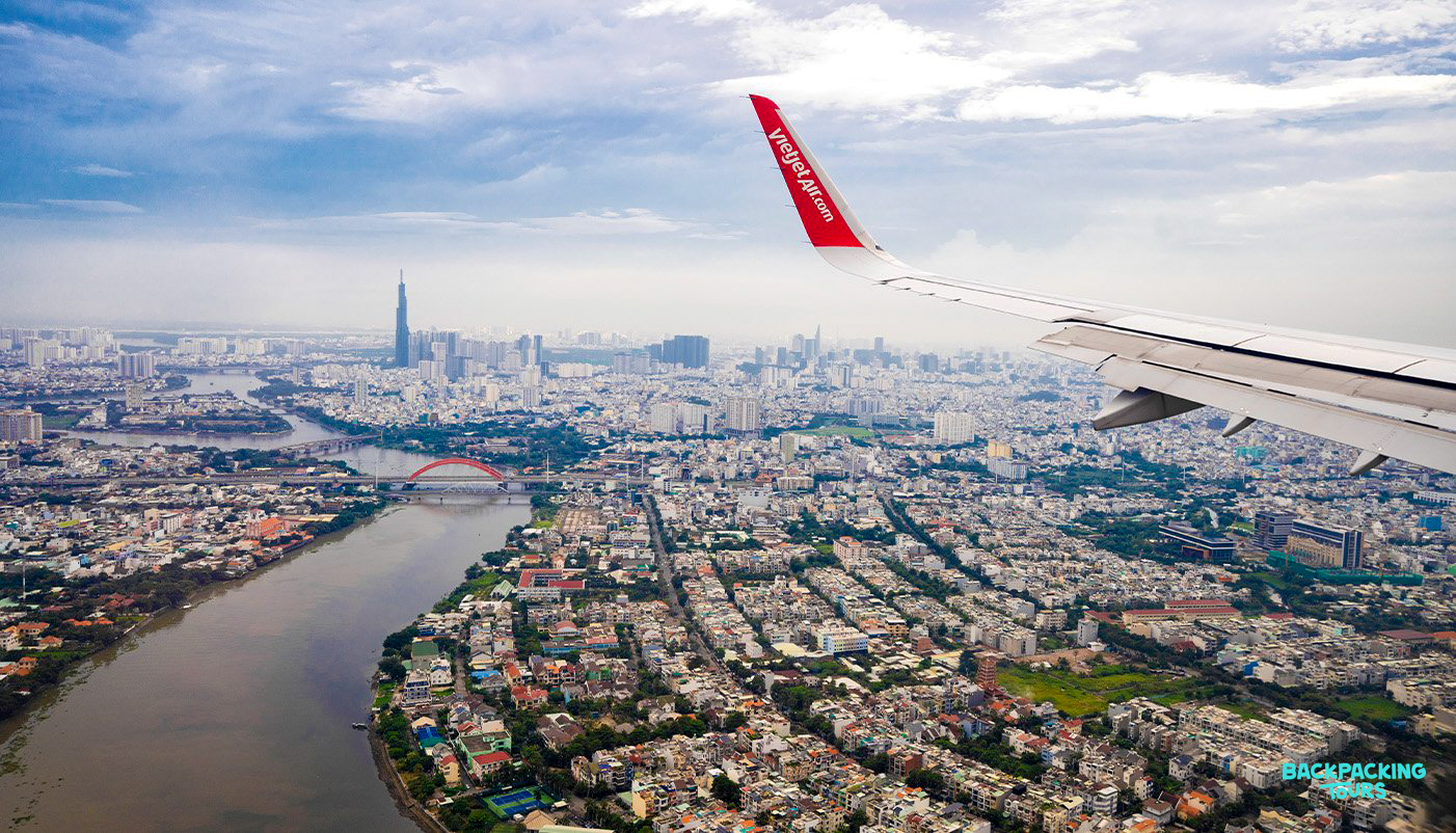 Aerial view of bustling Ho Chi Minh City, with its winding river, city buildings, and a plane wing.