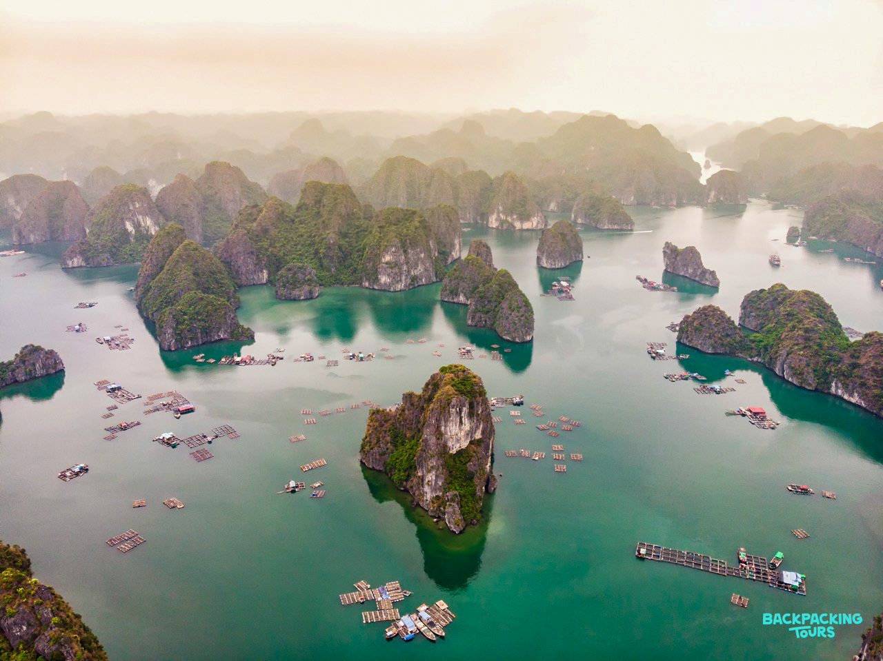 Ha Long Bay's majestic limestone karsts rise from emerald waters, dotted with numerous floating structures.