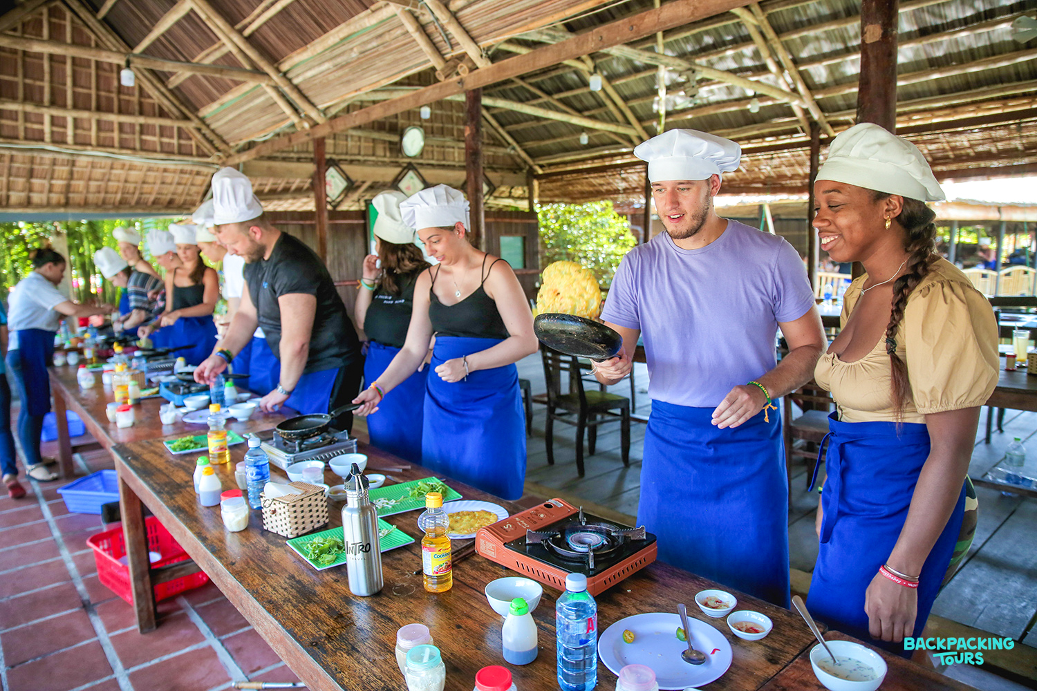 Tourists enjoy a hands-on Vietnamese cooking class in a rustic open-air kitchen in Hoi An.