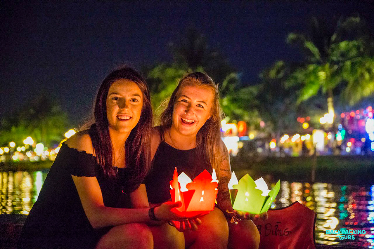 Two happy women hold vibrant lanterns, enjoying the illuminated river scene in Hoi An.