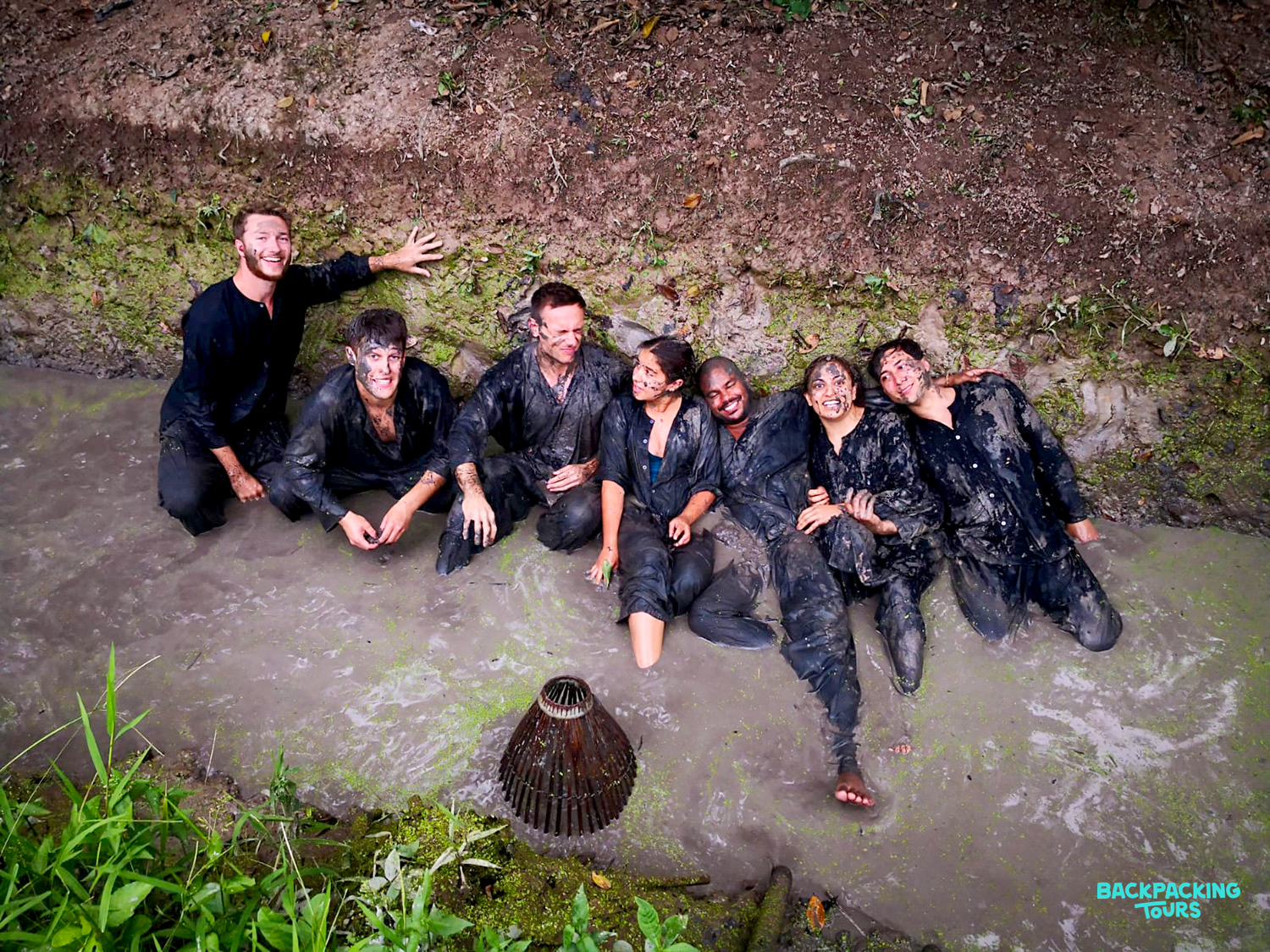 Seven happy backpackers covered in mud, enjoying a unique local experience in the Mekong Delta.