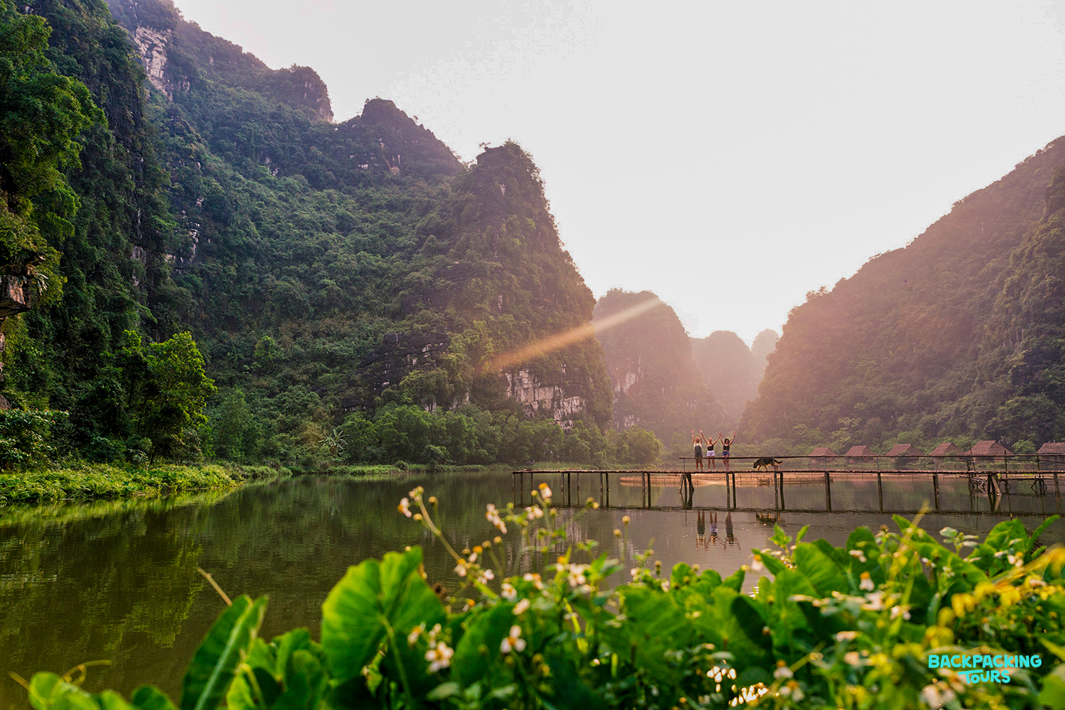 Golden sunset illuminates dramatic limestone mountains and a tranquil river with a bridge in Ninh Binh.
