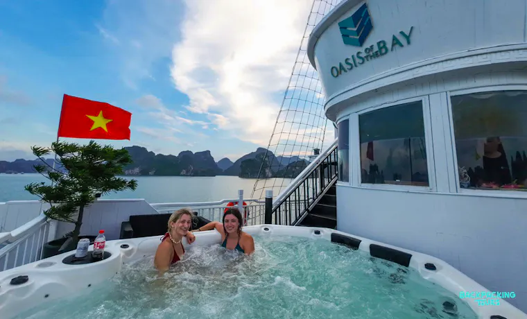 Friends relax in a hot tub on an overnight cruise, surrounded by stunning Ha Long Bay scenery.