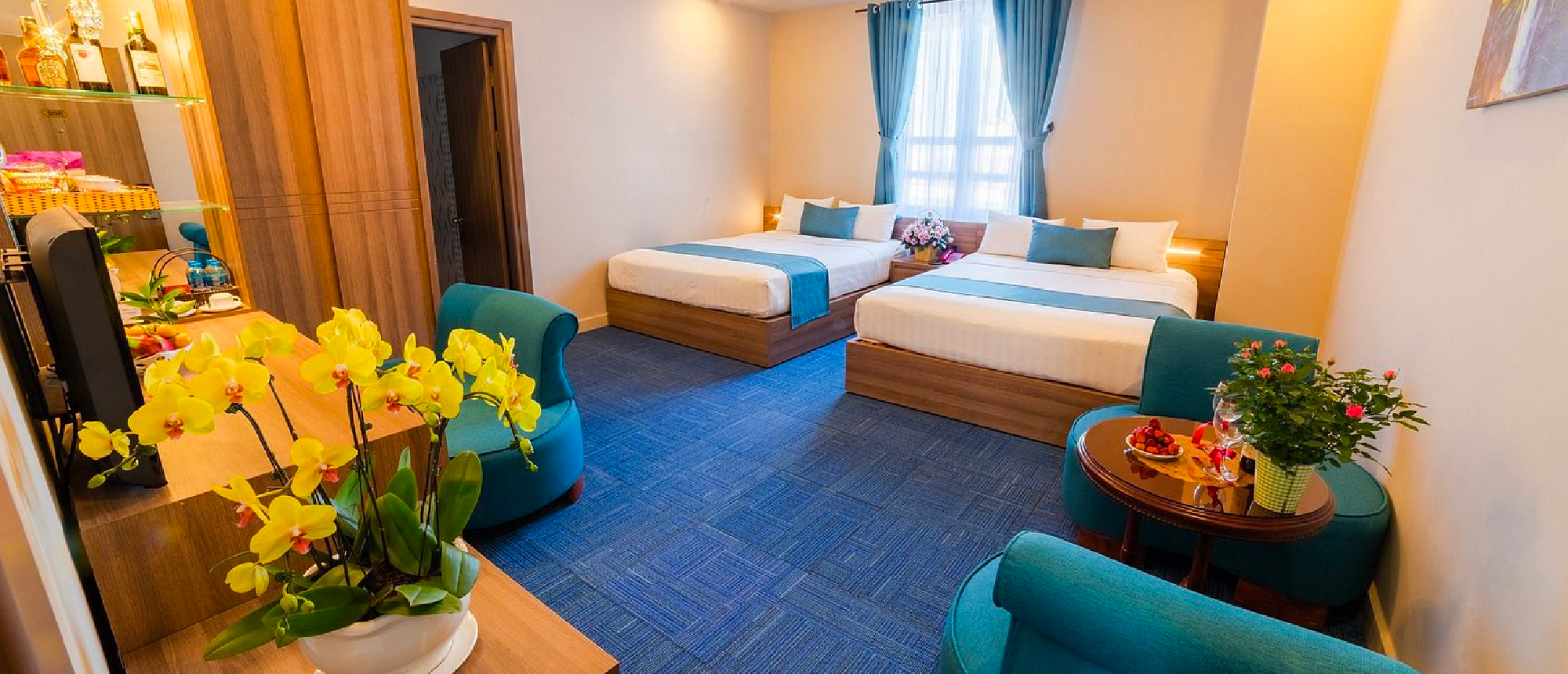A bright and comfortable hotel room with two beds, blue carpet, and a vibrant yellow orchid.