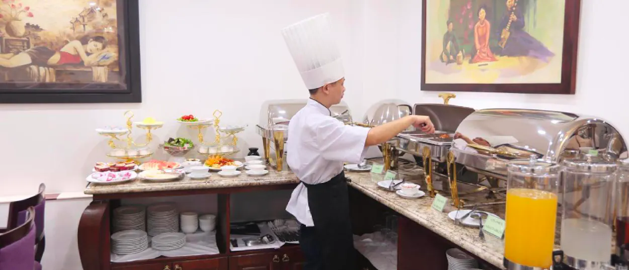 A chef in a white hat serves hot food from a breakfast buffet in Hanoi.