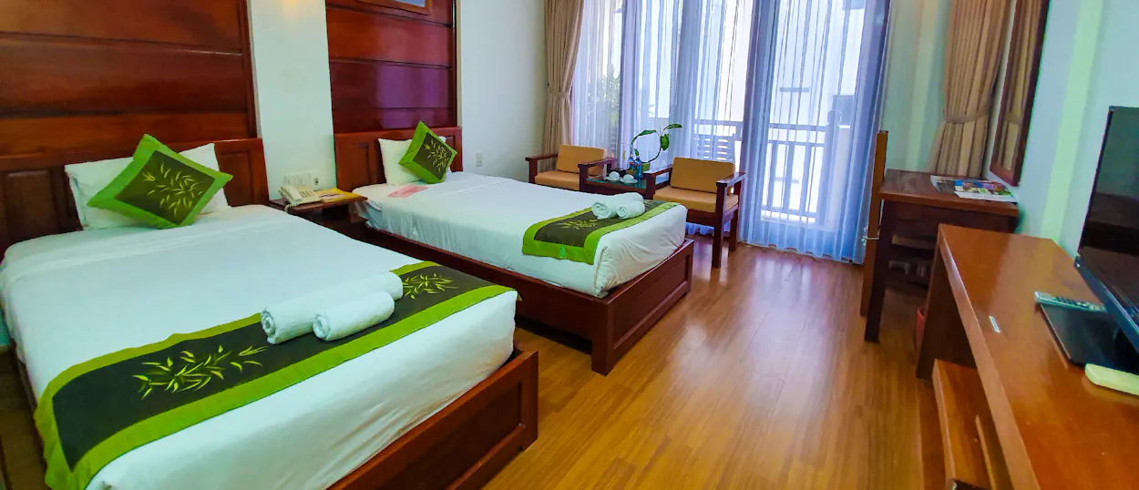 A bright, clean hotel room with two beds, wooden furniture, and a balcony for relaxation.