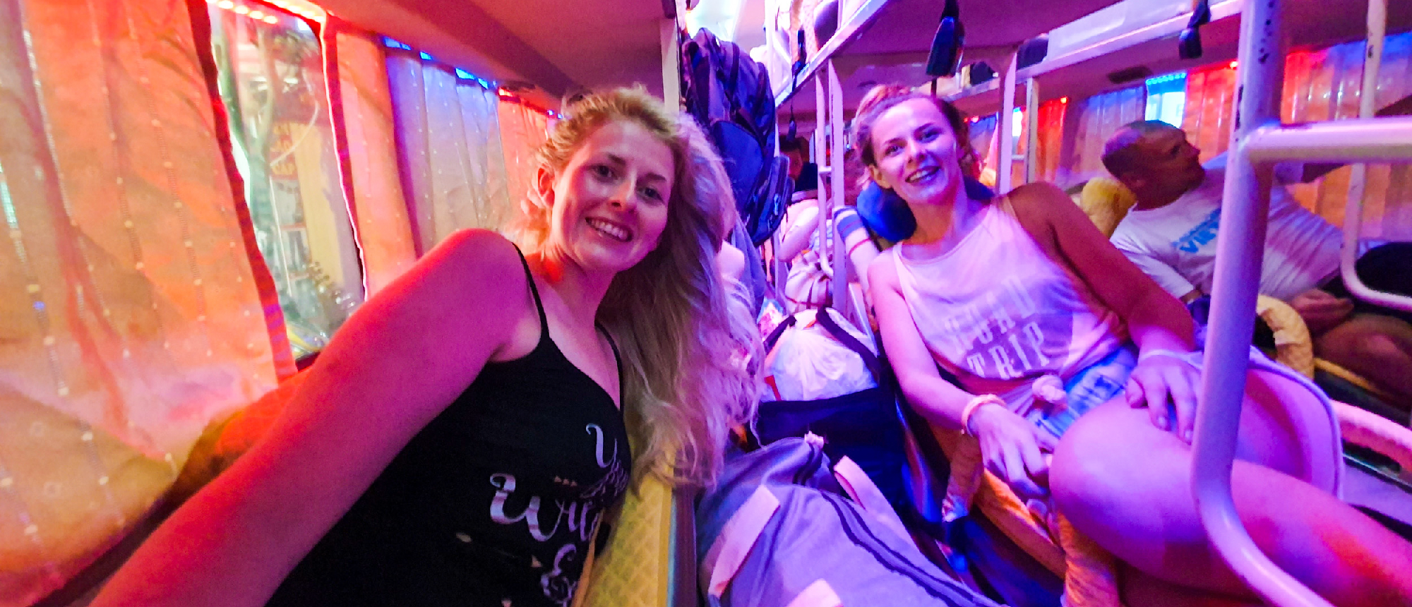 Two smiling women relax in their bunks on a colorful night bus in Vietnam.