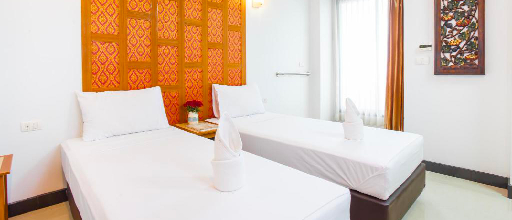 A simple twin hotel room in Bangkok with white beds, an orange patterned headboard, and a window.