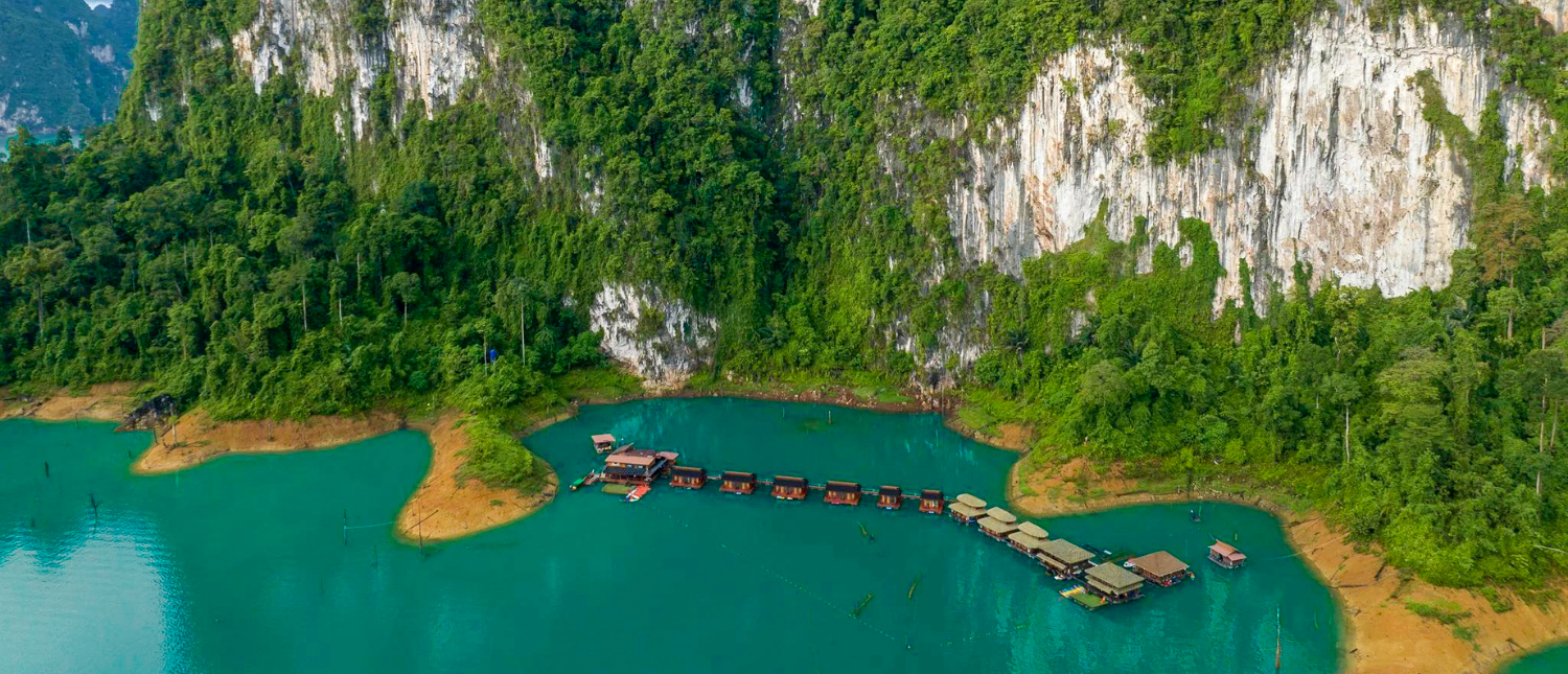 Floating bungalows on serene turquoise Cheow Lan Lake, Thailand, with towering jungle cliffs.
