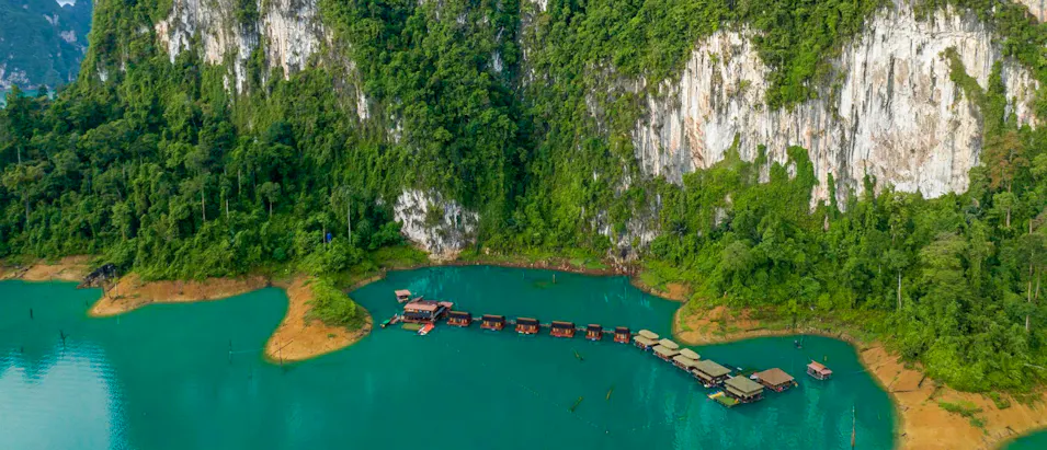 Floating bungalows on serene turquoise Cheow Lan Lake, Thailand, with towering jungle cliffs.